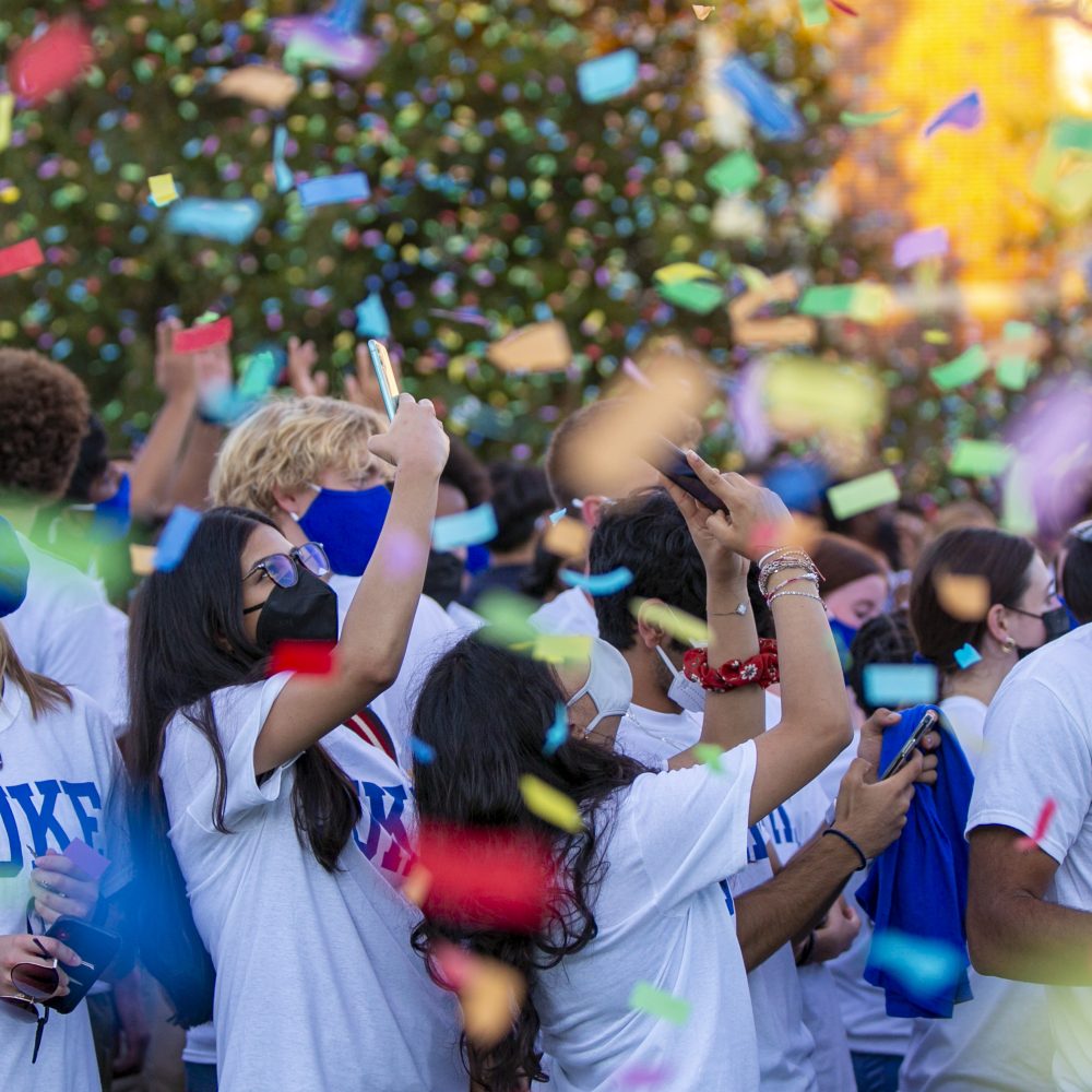 students in masks take photos of falling confetti