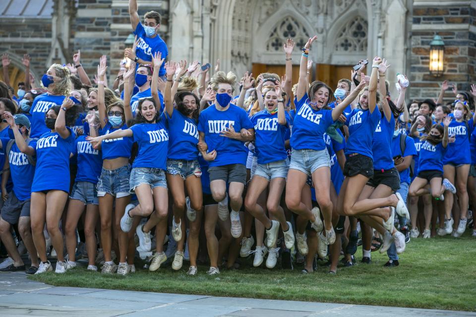 students in blue duke shirts mid-jump in front of the chapel