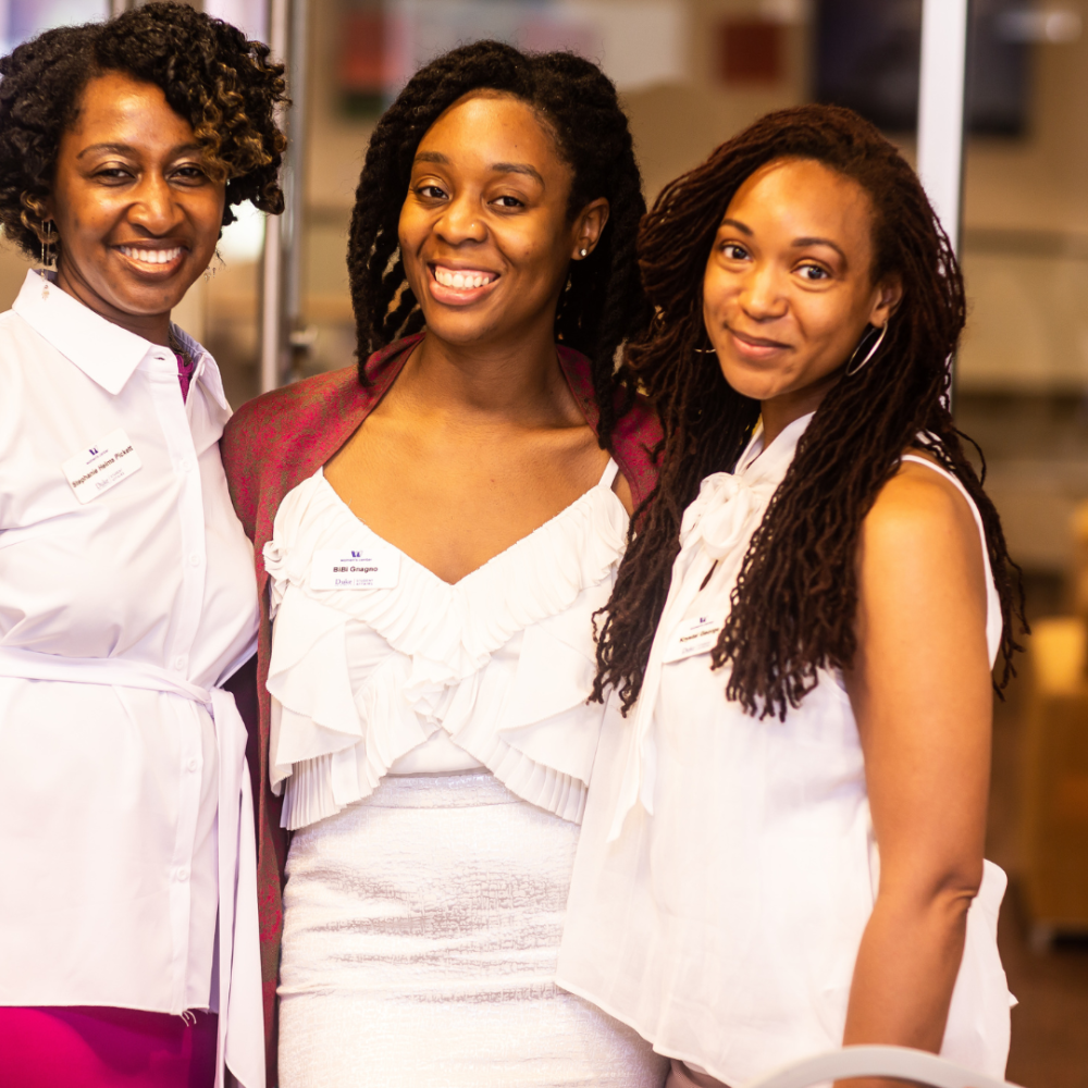 3 women of color wearing white outfits smiling at the camera