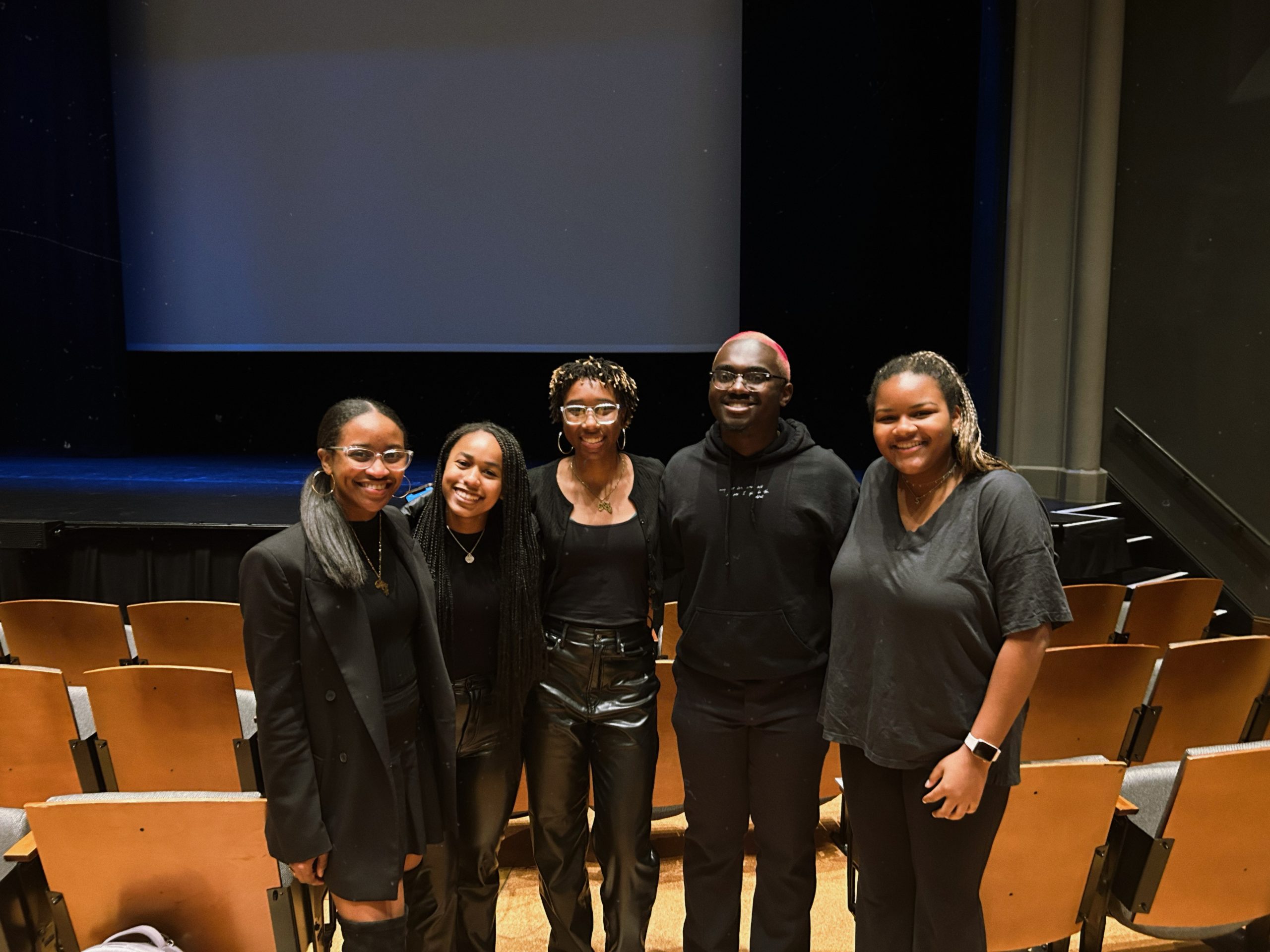 Five black students wearing all black smiling in page auditorium