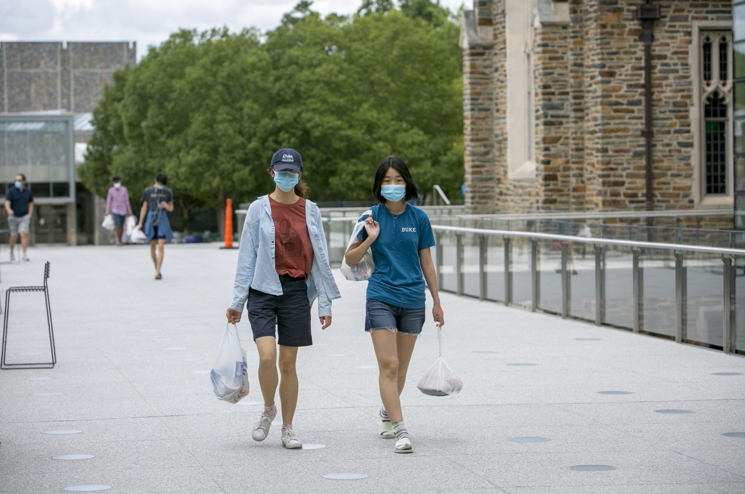 Wearing masks, juniors May Mei and Cindy Zhou walk across the Bryan Center Walkway with groceries from The Lobby Shop on West Campus.