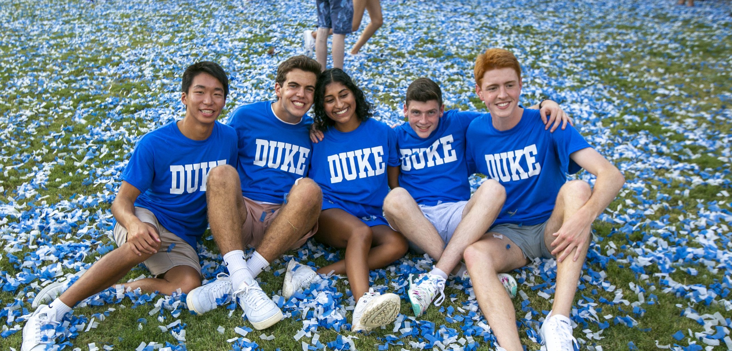 students sit in confetti with blue duke tshirts on
