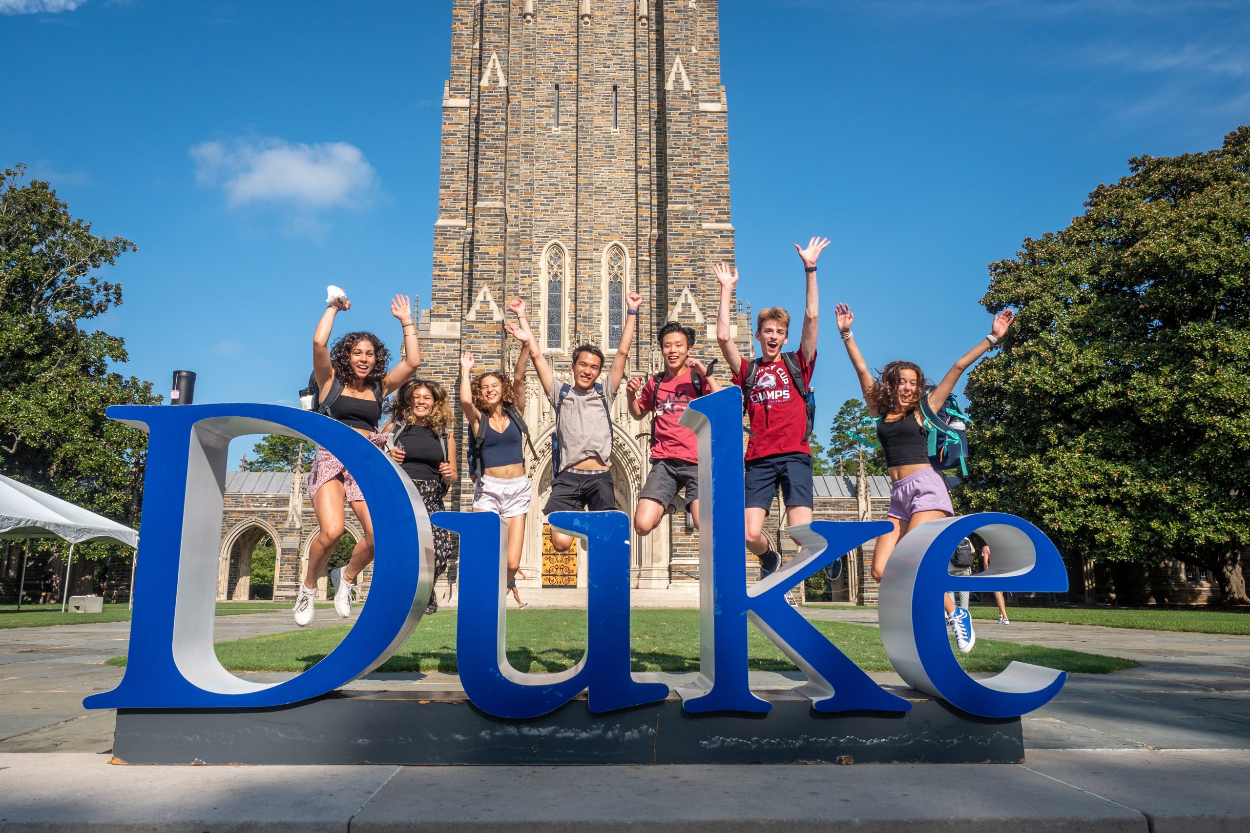 seven students jumping behind Duke sign in front of chapel