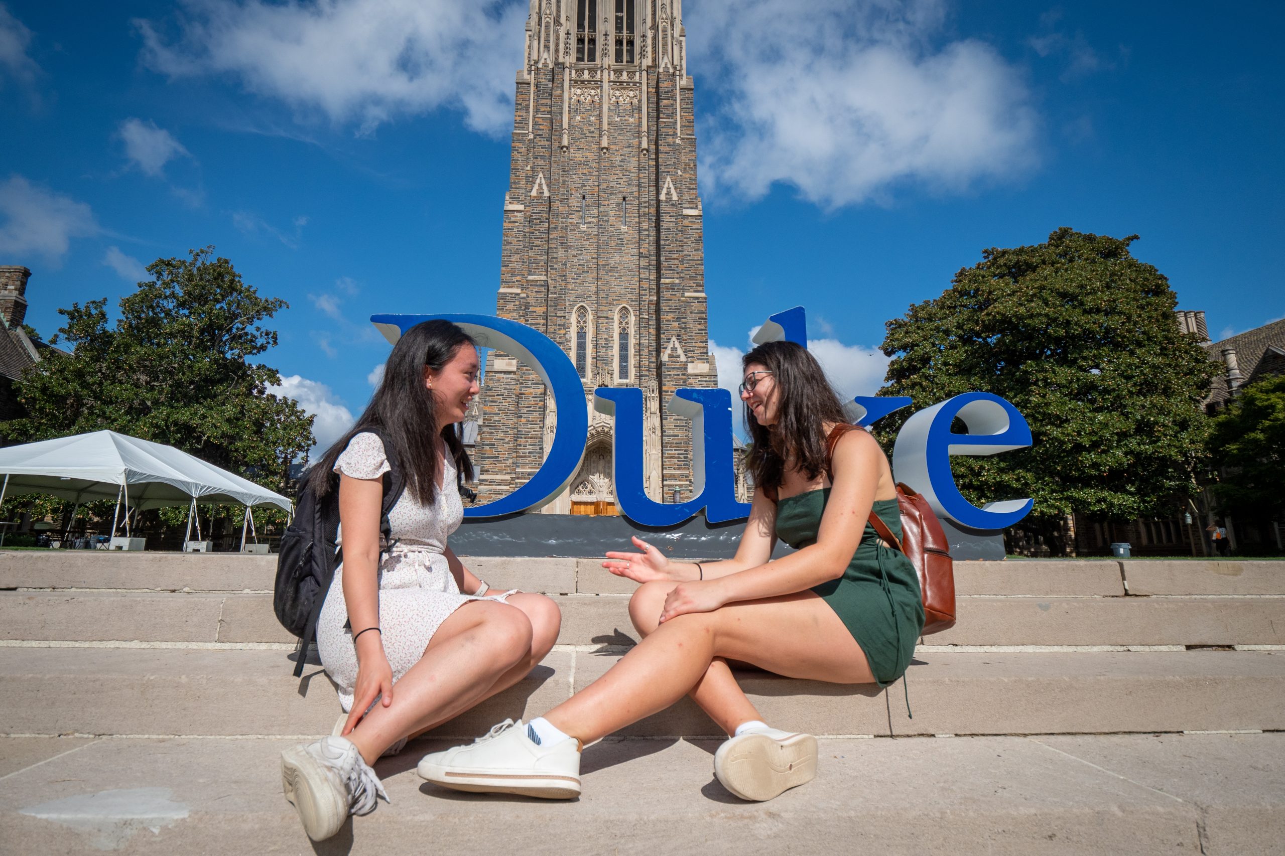 two students sit in front of a duke letter sign in front of the chapel