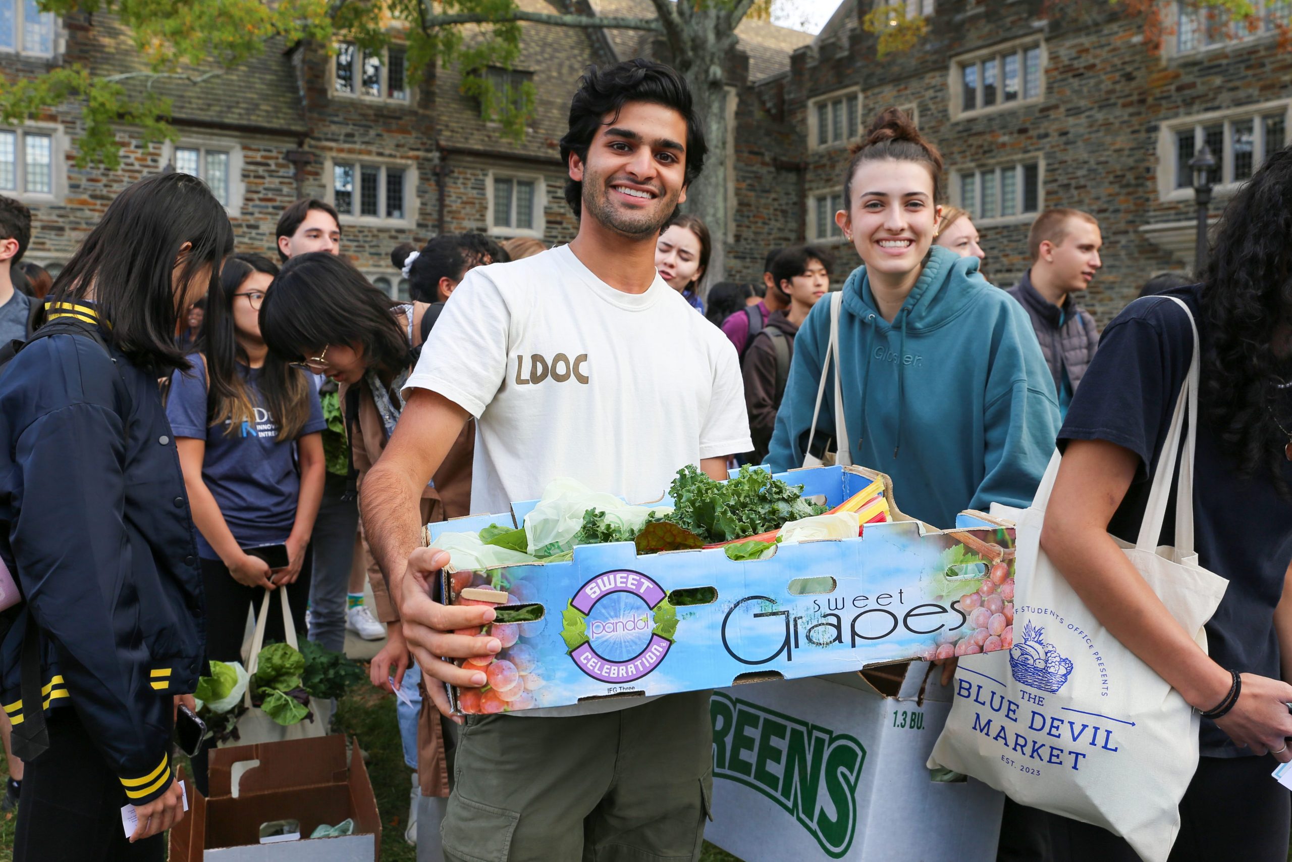 Two Duke students pose for the camera, holding boxes of fresh vegetables