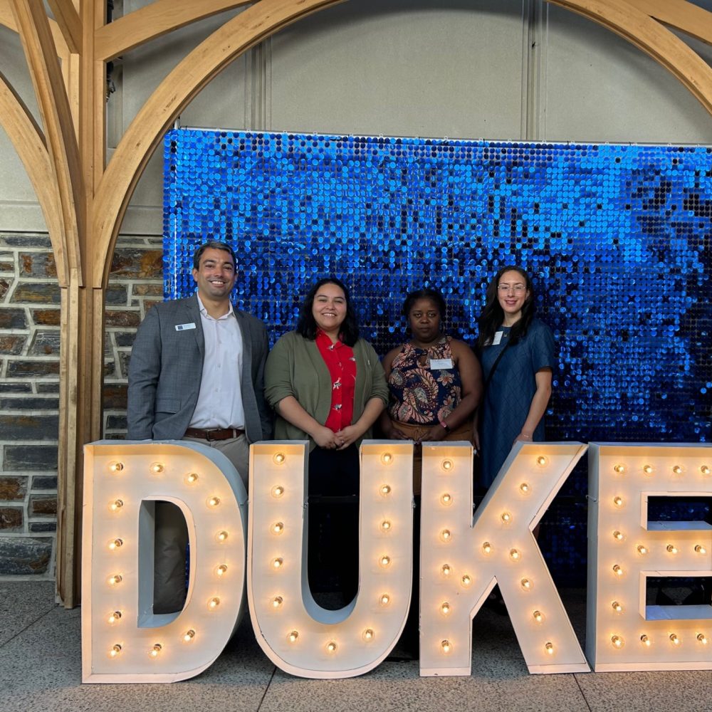 DISC staff posing behind the DUKE light-up sign